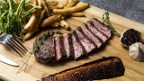 A cut of steak, fries and garlic on a wooden cutting board.