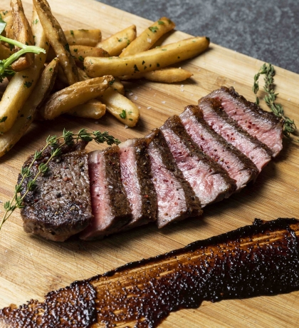 A cut of steak, fries and garlic on a wooden cutting board.