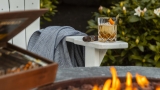 cocktail and a cigar sitting on a deckchair by a firepit