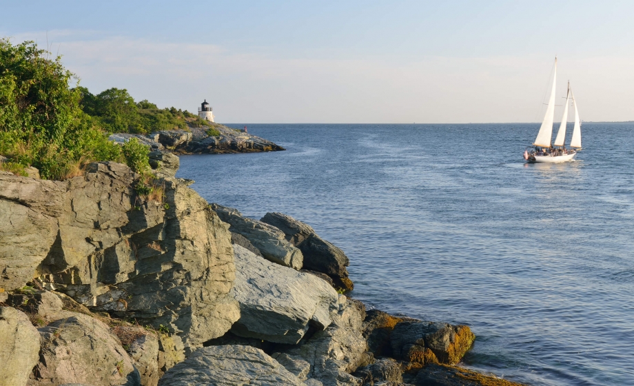 A sailing ship on the water with cliffs and a lighthouse in the background